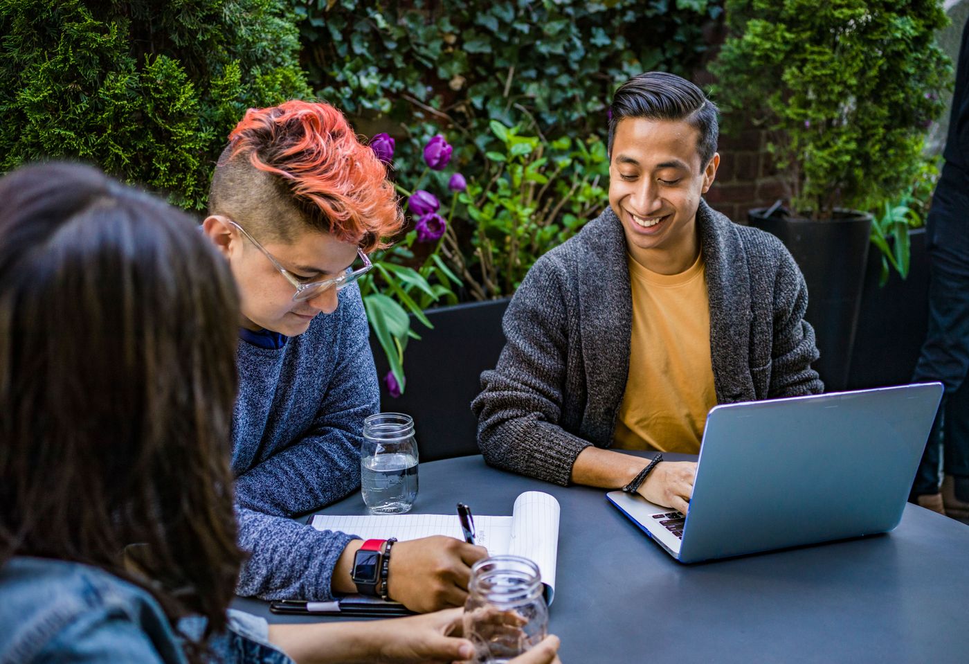 Drei Personen arbeiten im Freien gemeinsam an einem Tisch mit Laptop und Notizen